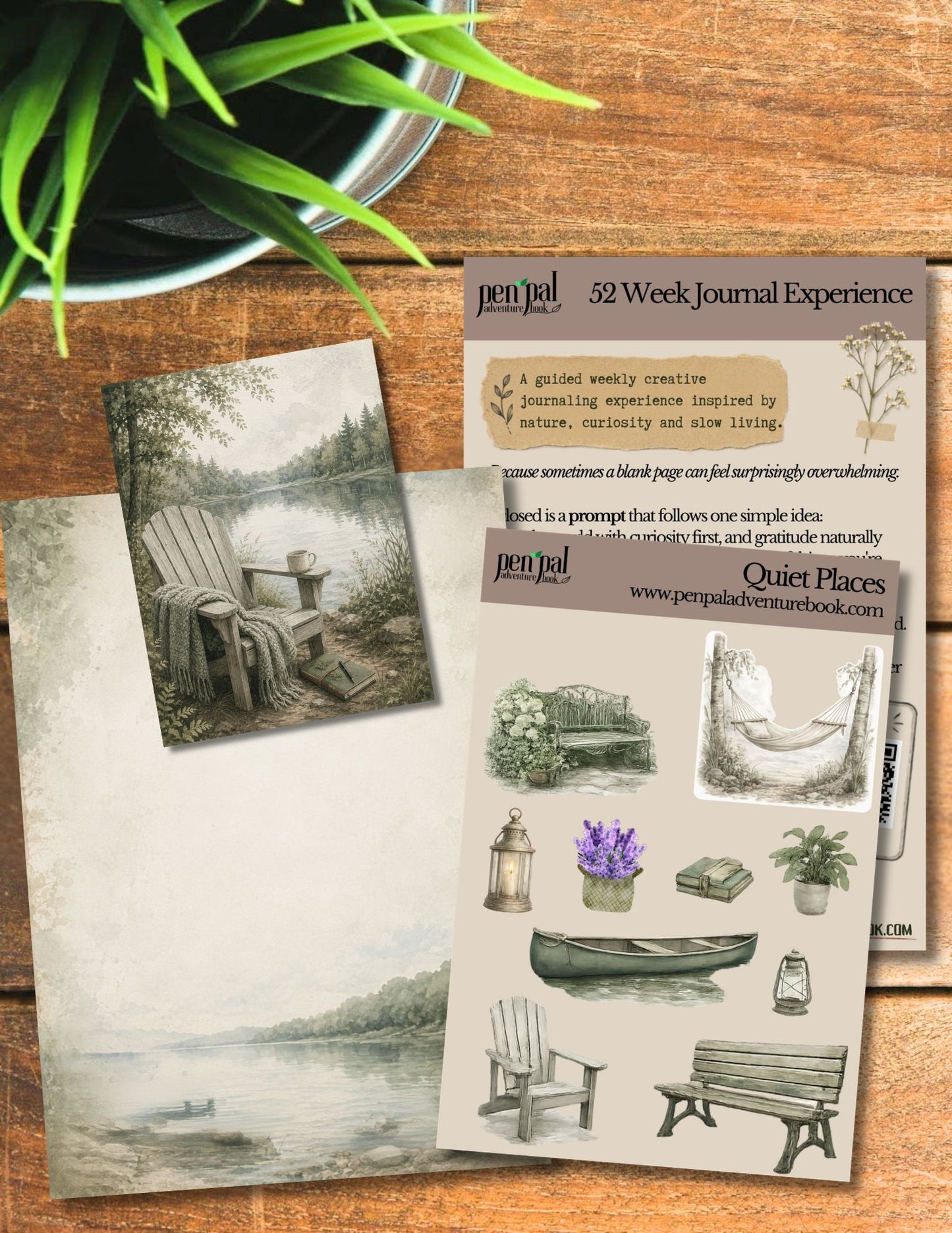A styled flat-lay of a journaling kit on a rustic wooden table, featuring a scenic lake illustration card, a stamp sheet labeled 'penpal 52 Week Journal Experience' and 'Quiet Places', and a stamp block, with a potted plant in the corner.