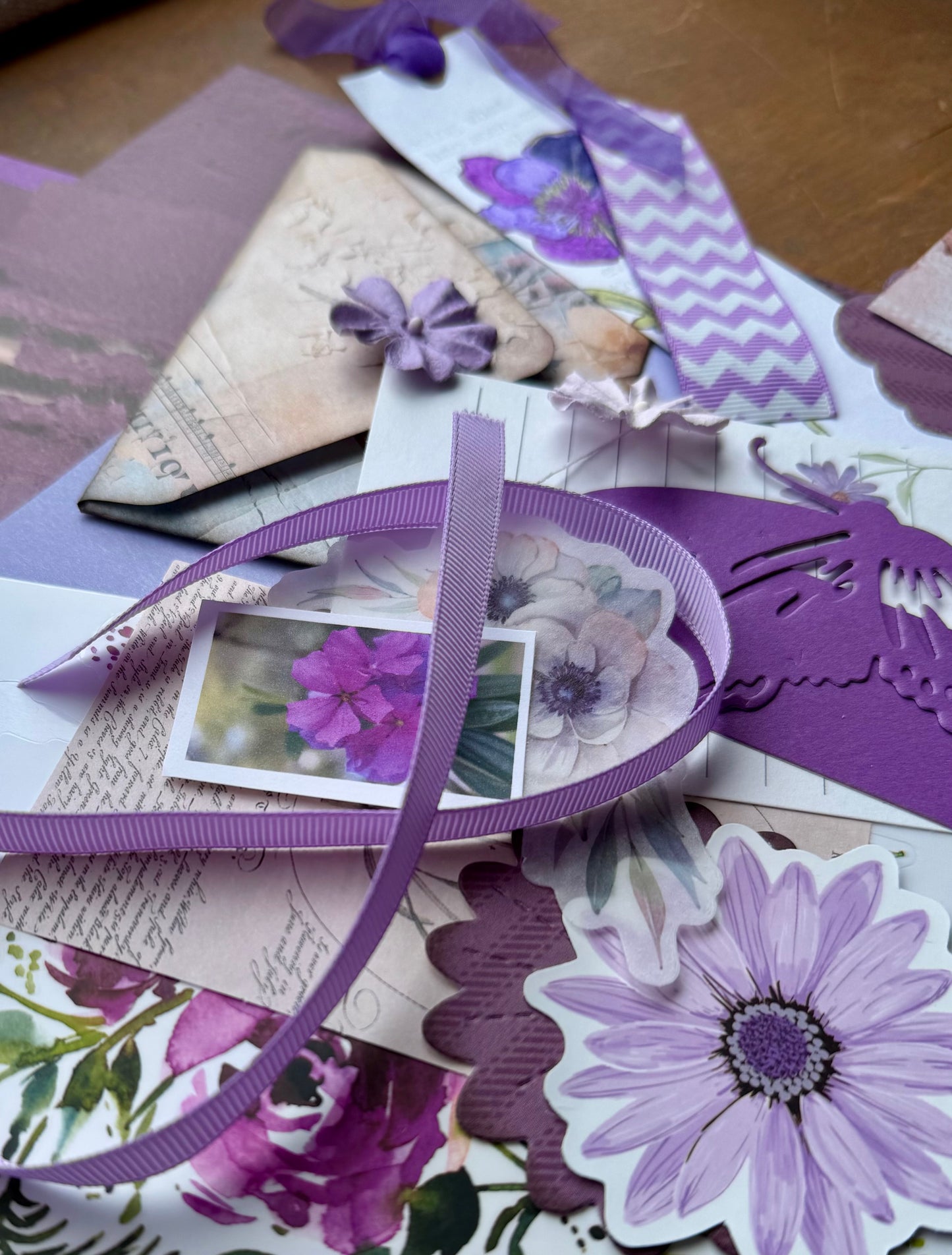 Scattered purple floral paper and ephemera pieces on a wooden surface
